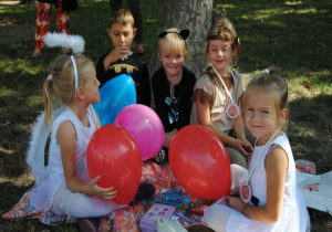 wesołe dzieci z balonami siedzą na kocu pod drzewem